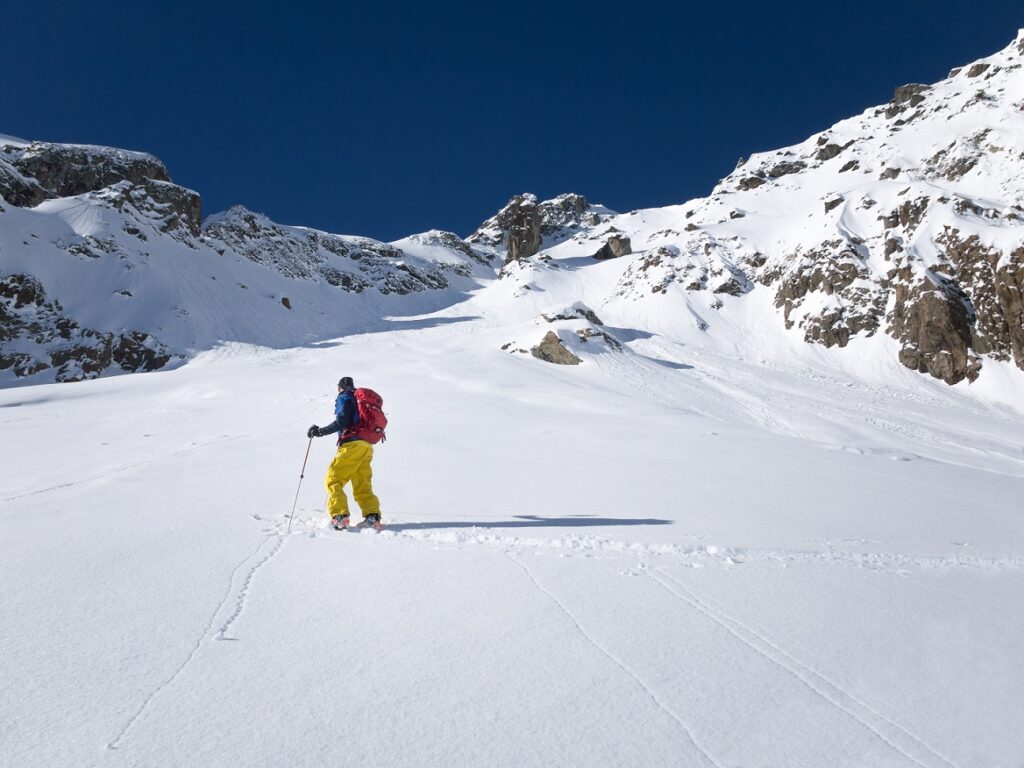 Skier,Walking,Up,Slope,In,Powder,Snow