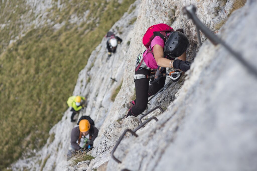 Woman,And,Group,Of,Other,People,Climbing,On,Steep,Rock